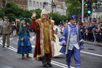 Na fotografii widać idących ulicą, przebranych za historyczne postacie, uczestników pochodu. Po obydwu stronach ulicy znajduje się tłum ludzi.