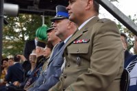 Na fotografii widać siedzących na trybunie uczestników pochodu. Wśród nich znajduje się Komendant Powiatowy Policji w Tarnowskich Górach insp. Krzysztof Hajda.