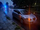 Na fotografii widać uszkodzony samochód osobowy. W tle fotografii widać policyjny radiowóz, który ma włączone światła błyskowe