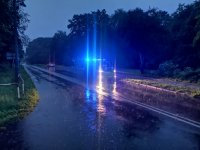 Na fotografii widać drogę, na której zaparkowany jest policyjny radiowóz z włączonymi światłami błyskowymi.