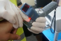 Na fotografii widać dłonie, na których założone są rękawiczki ochronne. W dłoni znajduje się urządzenie do ściągania odbitki linii papilarnych.