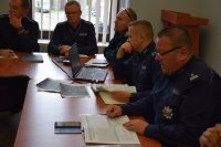 Na fotografii widać siedzących przy stolikach policjantów podczas odprawy służbowej. Odprawę prowadzi m.in. Pierwszy Zastępca Komendanta Powiatowego Policji w Tarnowskich Górach podinsp. Sławomir Bylicki