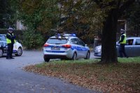 Na fotografii widać skrzyżowanie, przy którym stoi policyjny radiowóz, a obok niego znajdują się dwaj policjanci.