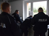 Na fotografii widać czterech odwróconych tyłem policjantów. Mundurowi przez okno obserwują stadion piłkarski.
