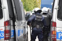 Na fotografii widać odwróconych tyłem policjantów, którzy przemieszczają się pomiędzy dwoma zaparkowanymi radiowozami.