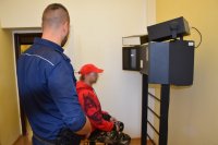 Na fotografii widać odwróconego policjanta. Obok niego, na krześle siedzi zatrzymany mężczyzna, przed którym znajduje się specjalistyczny aparat fotograficzny.