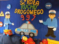 Na fotografii widać wycięty z papieru: napis &quot;szkoła ruchu drogowego 997&quot; Po obydwu stronach napisu widać policjantów, znaki drogowe, a pod napisem znajduje się radiowóz.