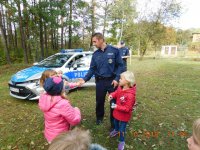 Na fotografii widać policjanta, który przybija &quot;piątkę&#039; z jednym z dzieci. W tle widać policyjny radiowóz.