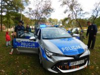 Na fotografii widać radiowóz, obok którego stoją policjanci oraz grupa dzieci