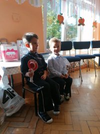 Na fotografii widać siedzących na ławce dwóch chłopców. Jeden z nich trzyma w dłoni lizak z napisem STOP