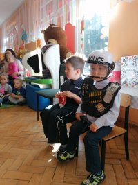 Na fotografii widać dwóch siedzących na ławce chłopców. Ubrani są w policyjne mundury.