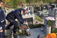 Na fotografii widać cmentarz, na którym znajduje się Komendant Powiatowy Policji w Tarnowskich Górach insp. Krzysztof Hajda. Komendant stawia na pomniku zapalony znicz. Na zdjęciu widać również kapelana policji diecezji gliwickiej ks. Joachima Gondro.