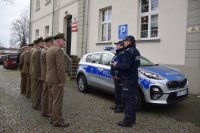 Na fotografii widać budynek Komisariatu Policji w Tworogu, przed którym znajduje się policyjny radiowóz, przy którym stoją: Pierwszy Zastępca Komendanta Powiatowego Policji w Tarnowskich Górach podinsp. Sławomir Bylicki, Komendant Komisariatu Policji w Tworogu, Wójtowie Gmin w Tworogu i Krupskim Młynie oraz przedstawiciele Nadleśnictw.