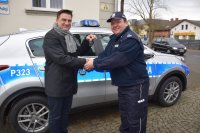Na fotografii widać policyjny radiowóz, przed którym Pierwszy Zastępca Komendanta Powiatowego Policji w Tarnowskich Górach podinsp. Sławomir Bylicki otrzymuje od Wójta Gminy Tworóg kluczyki do radiowozu.