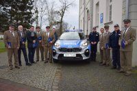 Na fotografii widać policyjny radiowóz, dookoła którego stoją: Pierwszy Zastępca Komendanta Powiatowego Policji w Tarnowskich Górach podinsp. Sławomir Bylicki, Komendant Komisariatu Policji w Tworogu, Wójtowie Gmin w Tworogu i Krupskim Młynie oraz przedstawiciele Nadleśnictw.