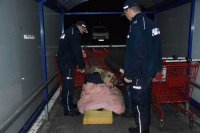 Na fotografii widać wiatę przeznaczoną do przechowywania koszyków sklepowych, pod którą dwóch policjantów oraz pracownik socjalny stoją przed legowiskiem osoby bezdomnej.