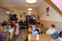 Na fotografii widać siedzące przy stołach osoby. W le zdjęcia widać policjantów, jeden z nich trzyma w ręku mikrofon