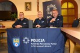 Na fotografii widać trzech siedzących przy stole policjantów . Jeden z nich trzyma w ręku mikrofon.