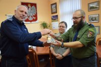 Na fotografii widać od lewej Komendanta Powiatowego Policji w Tarnowskich Górach insp. Krzysztofa Hajdę oraz harcerza, który przekazuje komendantowi Betlejemskie Światło Pokoju. Za mężczyznami stoi harcerka.