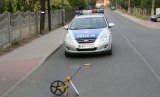 Na fotografii widać drogę, na środku której znajduje się policyjny radiowóz. Przed radiowozem, na jezdni widać przyrząd do pomiarów odległości.