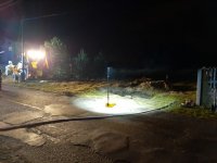 Na fotografii widać drogę, przy której stoi lampa oświetlająca dziurę w ziemi. Z lewej strony fotografii widać koparkę.