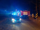 Na fotografii widać policyjny radiowóz oraz wóz strażacki, które zaparkowane są na drodze. W radiowozie włączone są światła błyskowe.
