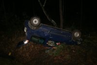 Na fotografii widać leżący na dachu samochód osobowy. Pojazd ma otwartą tylną klapę.