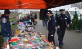 Z lewej strony fotografii widać stragany. Na stołach porozkładane są różne przedmioty. Obok stołu stoi mężczyzna. Z prawej strony zdjęcia widać dwóch policjantów oraz innych ludzi oglądających towar znajdujący się na stołach.