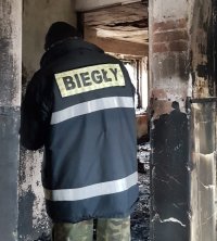 Na fotografii widać pomieszczenie, w którym znajduje się odwrócony tyłem mężczyzna. Na kurtce, na plecach widnieje napis BIEGŁY