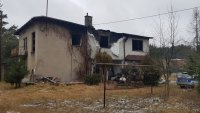 Na fotografii widać budynek, który jest częściowo spalony. Obok budynku widać zaparkowany policyjny radiowóz.
