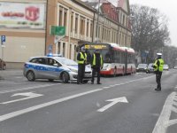 Na fotografii widać skrzyżowanie, na którym obok radiowozu stoją trzej policjanci. Za policjantami widać autobus oraz kilka samochodów osobowych.