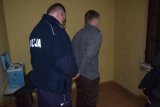 Na fotografii widać dwóch mężczyzn -policjanta i zatrzymanego. Policjant zapina kajdanki sprawcy