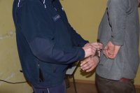 Na fotografii widać dwóch mężczyzn -policjanta i zatrzymanego. Policjant zapina kajdanki sprawcy