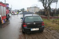 Na fotografii widać ulicę, na której widać tył zaparkowanego samochodu osobowego. Z jego lewej strony widać wóz strażacki, a w oddali dwa policyjne radiowozy i stojących obok nich kilka osób