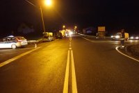 Na fotografii widać skrzyżowanie ulic. Z lewej strony zdjęcia widać policyjny radiowóz oraz zaparkowane na poboczu samochody osobowe i wóz strażacki. Z prawej strony zdjęcia widać strażaka oraz samochód osobowy