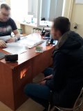 Na fotografii widać siedzących po obu stronach biurka dwóch mężczyzn. Na biurku widać m.in. dokumentację oraz zabezpieczoną przez policjantów gotówkę