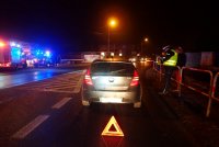 na drodze stoi zaparkowany pojazd. Przed samochodem widać trójkąt ostrzegawczy. Po prawej stronie zdjęcia widać policjanta wykonującego czynności, a po lewej radiowóz z włączonymi światłami błyskowymi.