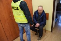 policjant stoi obok zatrzymanego, który siedzi na krześle