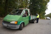 Na fotografii widać samochód dostawczy, obok którego stoi policjant. W tle fotografii widać policyjny radiowóz.