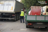 Na fotografii widać parking, na którym zaparkowane są ciężarówki, a pomiędzy nimi znajduje się policjant, który sprawdza stan techniczny pojazdów