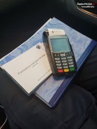 Na fotografii widać książkę, na której leży bloczek mandatowy oraz terminal płatniczy