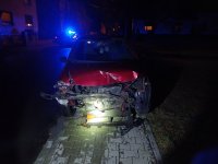 Na zdjęciu widać rozbity przód samochodu osobowego, w tle zdjęcia widać policyjny radiowozu, który ma włączone sygnały świetlne