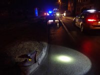 Na fotografii widać drogę, na której znajdują się policyjny radiowóz, wóz strażacki, samochód biorący udział w wypadku oraz zaparkowane na poboczu inne samochody.  Przy krawężniku drogi widać urwany element od jednego z samochodów.