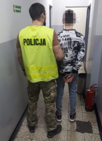 na fotografii widać policjanta, który trzyma za rękę zatrzymanego mężczyznę.