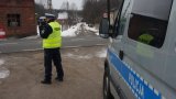 Na fotografii widać policjanta, który ma przystawione do twarzy urządzenie służące do pomiaru prędkości. Z prawej strony zdjęcia widać bok policyjnego radiowozu