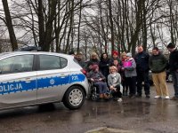 Na fotografii widać policyjny radiowóz,  obok którego stoją osoby niepełnosprawne, ich opiekunowie. Wśród nich znajduje się dzielnicowy