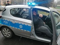 policyjny radiowóz, wewnątrz którego na fotelu pasażera siedzi mężczyzna
