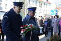 fotografia kolorowa.  Pierwszy Zastępca Komendanta Powiatowego Policji w Tarnowskich Górach podinsp. Sławomir Bylicki wraz z Dyrektorem Aresztu stoją  z wiązanką kwiatów i zapalonym zniczem