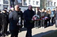 Przewodniczący Rady Miasta Tarnowskie Góry Adrian Wolnik trzyma wiązankę kwiatów. W tle zdjęcia widać grupę ludzi