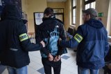 na zdjęciu: dwaj policjanci prowadzą zatrzymanego mężczyznę